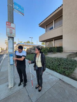 Ivan and Danyelle at the bus stop. Ivan is explaining the bus stop information sign and how it use the information to Danyelle.