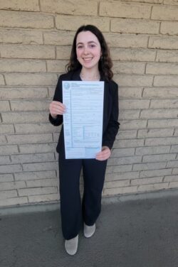 Systems Change Advocate BreeAnna holding voter’s registration form standing in front of beige brick wall smiling