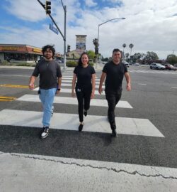 Pictured L-R DMC Travel Trainers Babar, Sol and DMC’s Lead Home and Community Access Coordinator Ivan walking across crosswalk on a sunny day.