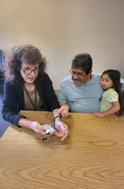 Pictured: Older adult consumer using AT Device Pocket Talker as Board VP and child look on to observe