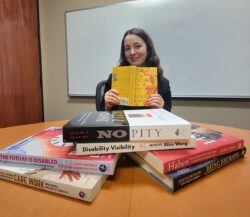 DMC’s Systems Change Advocate BreeAnna at DMC with advocacy books at table in conference room.