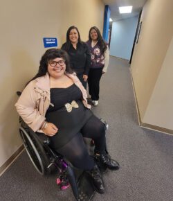 Pictured: DMC’s I&R Team -Nelly, Bianca and Paola in hallway with blue sign which reads “reception” with white arrow leading to the reception area.
