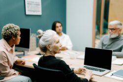 Group of older adults with younger adults participating in Assistive Technology Collaborative Group sitting at table with laptops