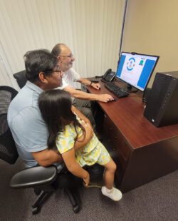 Pictured DMC Board VP sitting at desk showing Veteran how to access the Join Our Board page on computer
