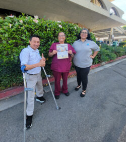 DMC’s PAS Recruitment Specialist, Kevin Dinh with caregiver (center) and Judith Garcia, DMC’s PAS Coordinator standing outside as caregiver holds Caregiver Recruitment flyer.