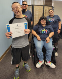 Pictured: Team DMC’s Alan, Nelly and Anita wearing DMC Summer Youth Academy shirts inside DMC with Summer Youth Academy participant Mason who was just presented a Youth Connect Award