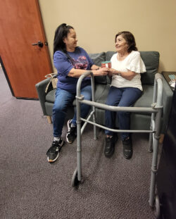 Caregiver with consumer sitting down as caregiver offers consumer a cup of tea in comfort