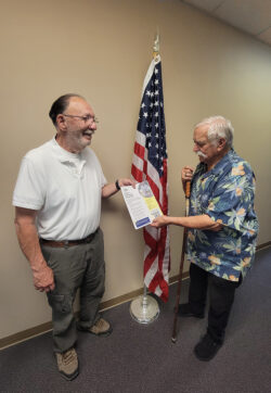 DMC’s Board President and Veteran Tony Clement handing VIP program flyer to fellow Veteran next to U.S. Flag at DMC
