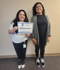 Pictured Volunteer Coordinator Raquel standing with Volunteer Daysi as Raquel holds a JOIN US TODAY sign with DMC LOGO