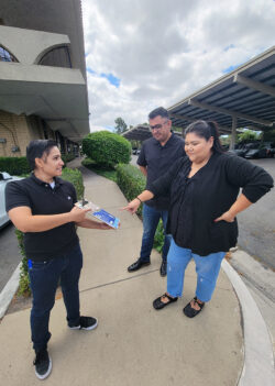 Ana holding DMC’s Home Access flyer showing it to Ivan and Esme as Esme points to contact information QR Code as they all stand outside