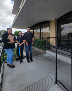 Home Access Team on ramp; Esme with clipboard; Ana with blue yard stick and Ivan holding tape measure outside of building
