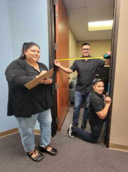 Pictured DMC Home Access Team: Esme standing by door holding clipboard taking measurement notes; Ivan in doorway with tape measure to review access width; Ana on knees in doorway side marking area with pen