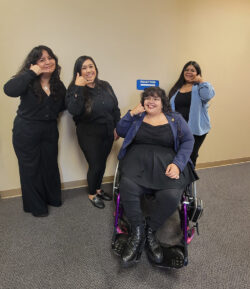 DMC’s I&R Team – Mareli, Bianca, Paola and Nelly signing “phone” in ASL in hallway with a blue sign which reads “reception” with white arrow leading to the reception area.