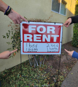DMC Housing pointing to red and white apartment for rent sign outside.