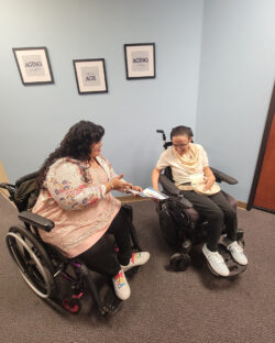 DMC Reception Volunteer Nina being peer-supported by Nelly as she explains flyer from reception.