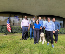 Group photo in front of DMC offices on lawn with U.S. flag in the background. Front row L-R: Marysol Cuadrado, Lead VIP Advisor, Michelle Ramos, Director of Community Support Services. Back row L-R Griffin Dooley, DMC Board Governance Chair with Service Dog Vivy, Tony Clement, DMC Board President, Eric Rodriguez, VIP Advisor, Riverside with Service Dog Honey, Andrew Toney, VIP Advisor Los Angeles and Luis Alvarez, DMC VIP Advisor OC/L.A.
