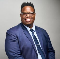 Head shot of Alvin who is wearing glasses and a blue suite and tie