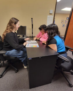 BreeAnna DMC Systems Change Advocate sharing information about intake with nelly and Mareli in office at desk