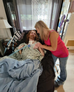 Transition consumer in his hospital bed with mother and primary caregiver at his bedside, holding his hand, and looking into his eyes lovingly.