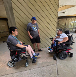 Three DMC Youth participants in group discussion in front of tan panel wall discussing advocacy and disability