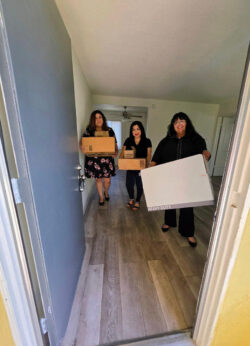 DMC Housing Team holding moving boxes with open door to new apartment