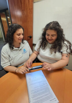 Wendy helping Gaby use magnifying AT device on document.